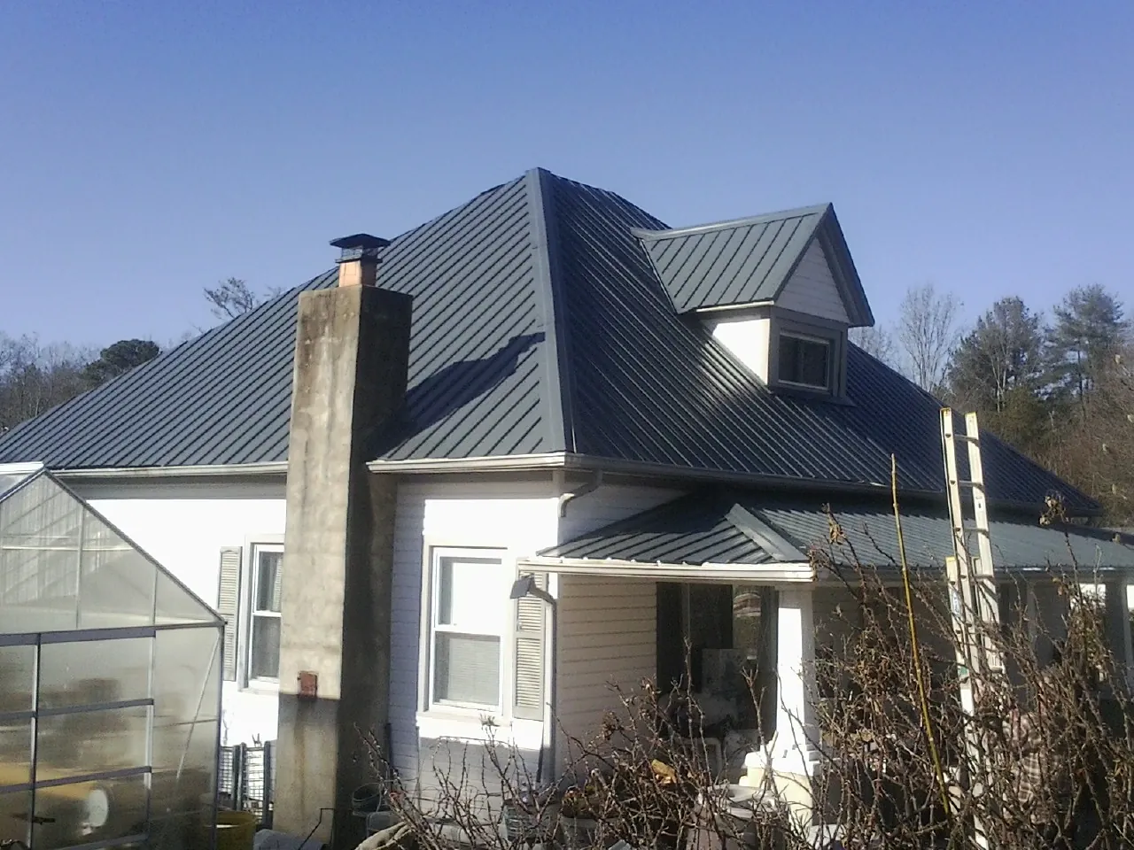 Dark blue standing seam metal roof on a white farmhouse with dormer — Slate & Tile Roof Repair by Roofing Brothers in West Yarmouth