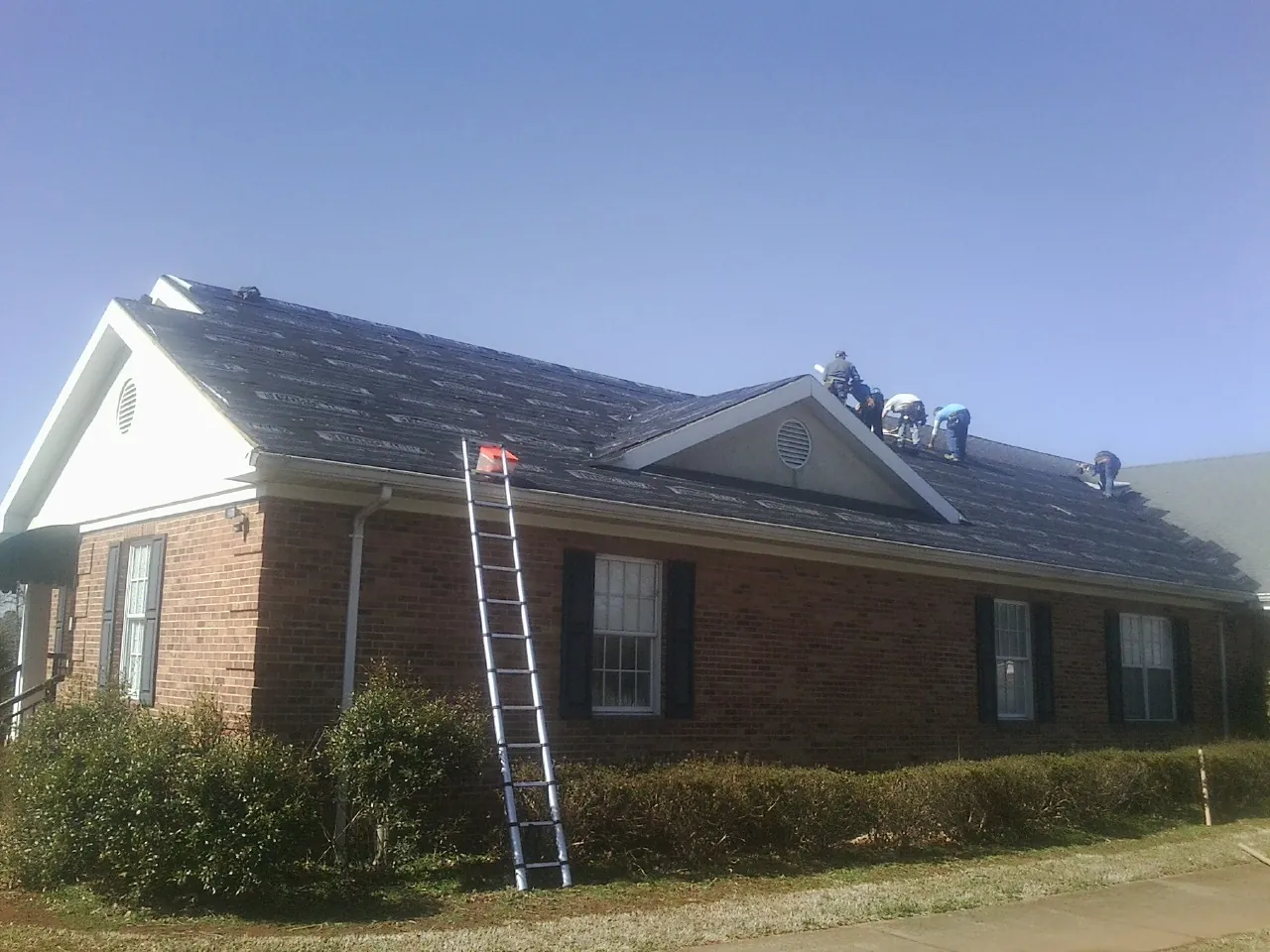 Crew tearing shingles off a brick ranch roof with a ladder set — Metal Roof Repair work by our crew in West Yarmouth
