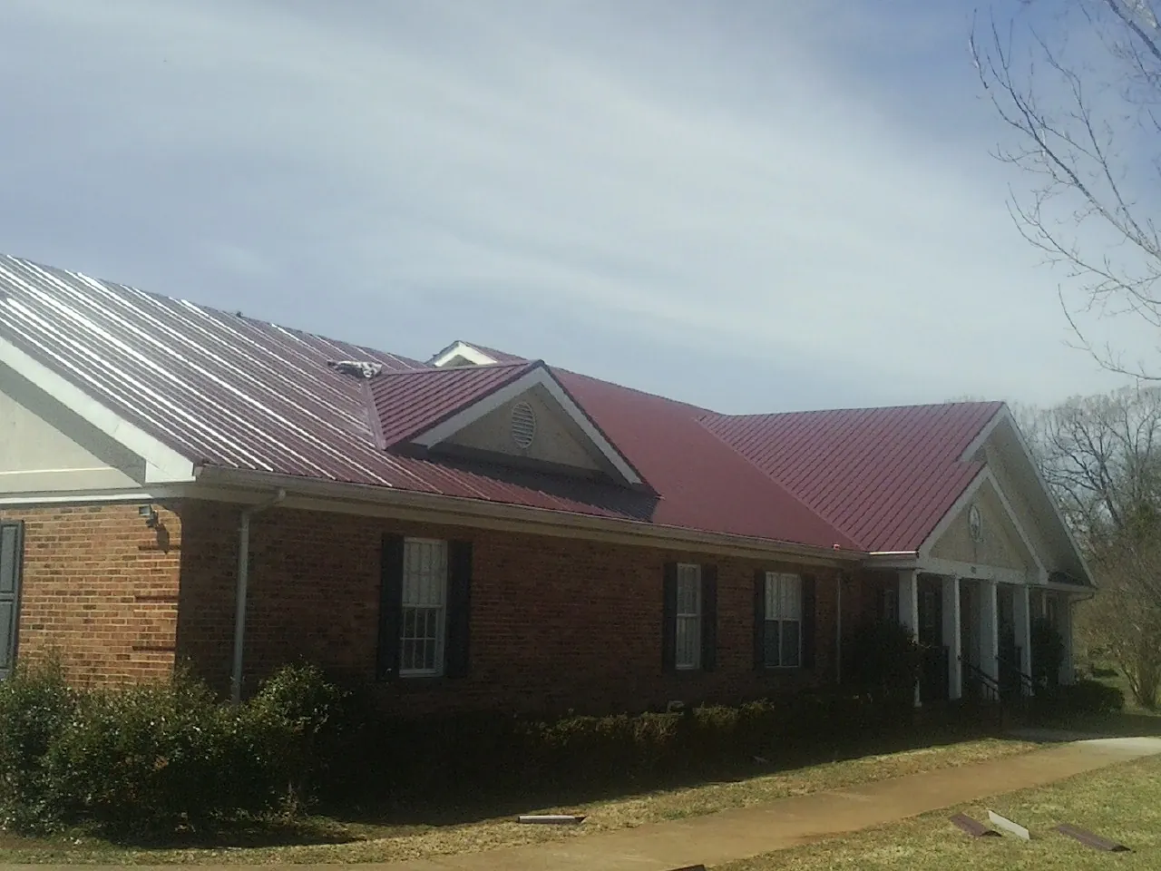 Red metal roof with gabled entries on a long brick building, from a Hail Damage Roof Repair job in West Yarmouth