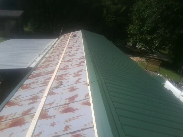 Old rusted panels beside newly installed green metal roofing — Wind Damage Roof Repair by Roofing Brothers in West Yarmouth