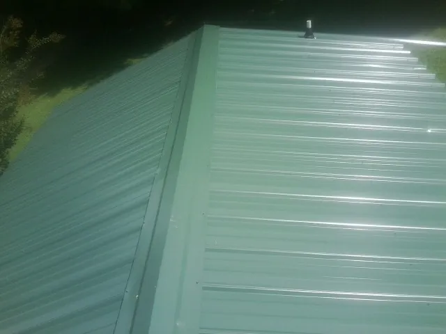 New green metal panels meeting at the ridge of a roof — Flat Roof Repair work by our crew in West Yarmouth