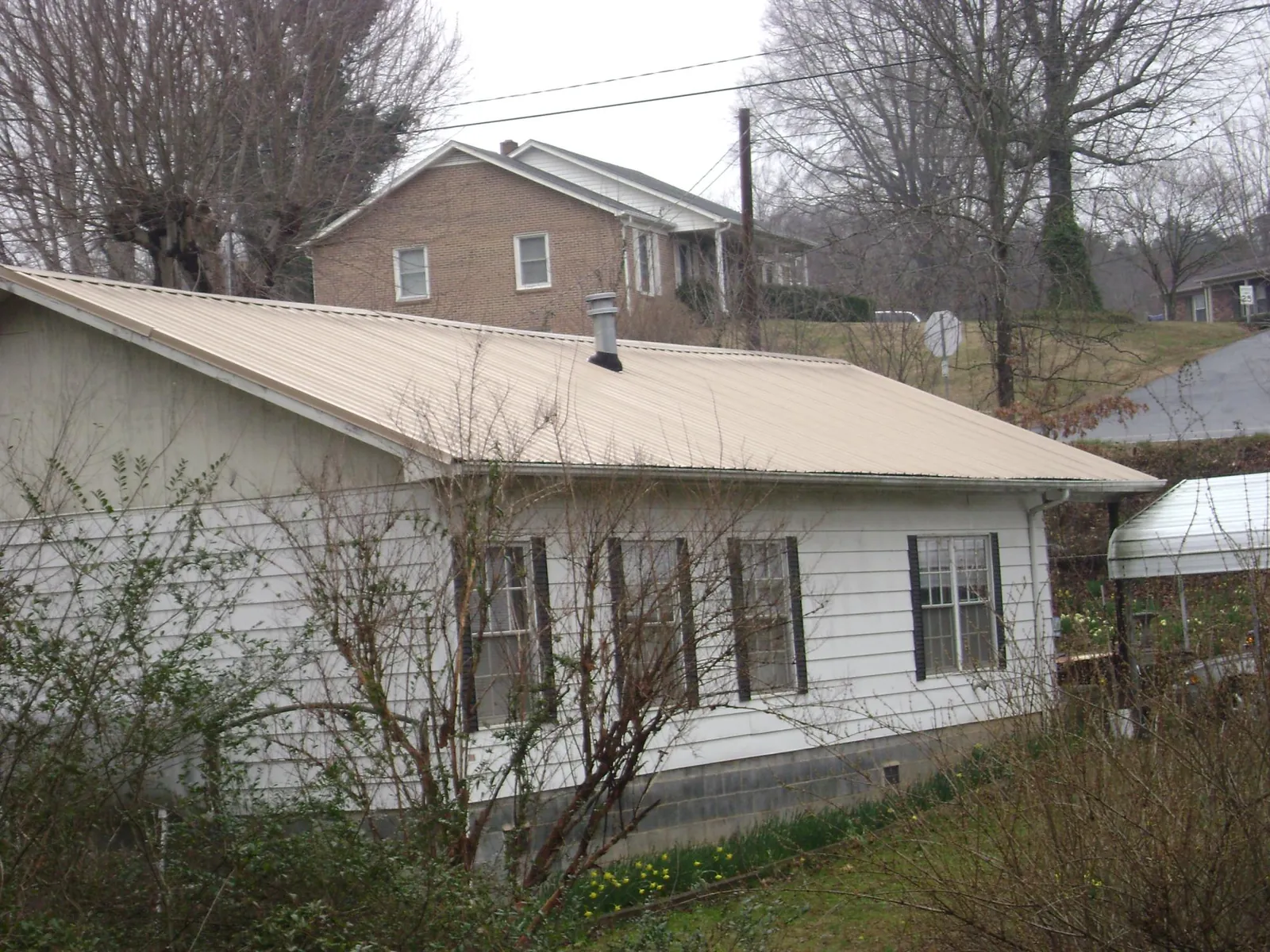 Tan metal roof on a white sided house set into a hillside — Commercial Roofing by Roofing Brothers in West Yarmouth